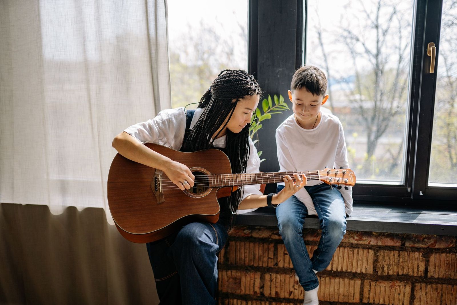 Lehrerin zeigt einem Jungen am Fenster die Gitarre